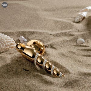Könnte beinhalten: Ein goldener Türgriff mit einem Spiraldesign und klaren Kristallen. Der Griff befindet sich auf einer sandigen Oberfläche.