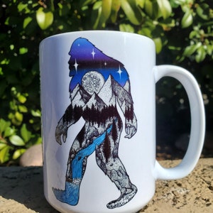 Pu&ograve; includere: Tazza in ceramica bianca con un design di Bigfoot. Il design presenta una silhouette di Bigfoot riempita con un cielo stellato, montagne e una cascata. La tazza ha un manico grande.