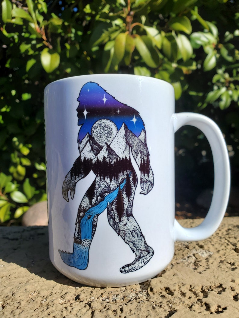 Pu&ograve; includere: Tazza in ceramica bianca con un design di Bigfoot. Il design presenta una silhouette di Bigfoot riempita con un cielo stellato, montagne e una cascata. La tazza ha un manico grande.