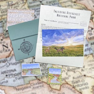 May include: A stationery set featuring a Theodore Roosevelt National Park information sheet, a sage green envelope with a compass rose stamp, a postcard of horses in a grassy field, a small landscape sticker, and a postage stamp-shaped sticker.