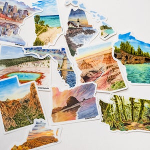 Può includere: Un set di dieci adesivi di contorno di stato ad acquerello che rappresentano vari paesaggi. Gli adesivi sono stampati su carta bianca e hanno una finitura lucida. Gli stati includono Minnesota, Michigan, Florida, Wyoming, Arizona, Oregon, Utah, Washington, Wisconsin e uno stato con una scena di foresta.