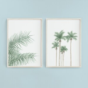 以下が含まれることがあります： 植物のイラストが描かれた額装されたプリントが2枚。左側のプリントは緑色のヤシの葉のクローズアップ。右側のプリントは緑色の葉をつけたヤシの木が5本並んでいる。