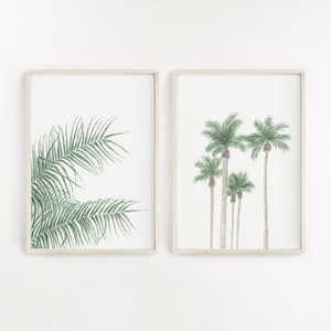 以下が含まれることがあります： 植物のイラストが描かれた額装されたプリントが2枚。左側のプリントは緑色のヤシの葉のクローズアップ。右側のプリントは緑色の葉を持つヤシの木が5本並んでいる。