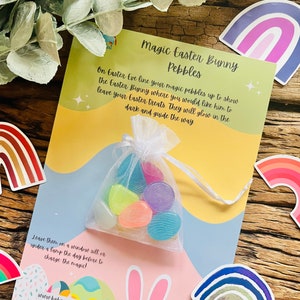 May include: A card with instructions for a magic Easter bunny activity. The card features a colourful illustration of an Easter bunny and a rainbow. The card also includes a small bag of glow-in-the-dark pebbles. The text on the card reads: "Magic Easter Bunny Pebbles. On Easter Eve line your magic pebbles up to show the Easter Bunny where you would like him to leave your Easter treats. They will glow in the dark and guide the way. Leave them on a window sill or under a lamp the day before to charge the magic! www.baba-too.co.uk Remember to leave me a carrot!"