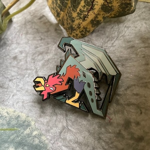 Puede incluir: Un pin de esmalte colorido que presenta un dragón estilizado con un cuerpo rojo, amarillo y morado y alas grises. El dragón está en una posición enroscada con la cabeza mirando hacia la izquierda.