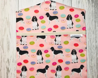 Peut inclure: Un sac à linge suspendu en tissu rose avec un cintre blanc. Le sac a un motif répété de chiens Springer Spaniel noirs et blancs et de beignets colorés. Le sac a une poche blanche avec le texte "jtaylorcrafts" imprimé dessus.