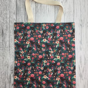 May include: A teal blue tote bag with a floral pattern featuring brown and white dogs. The bag has cream coloured straps.