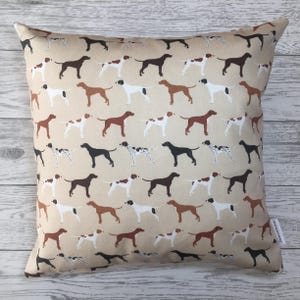 Può includere: Un cuscino beige con un motivo ripetuto di cani pointer marroni, neri e bianchi. I cani sono in varie pose, alcuni in piedi, alcuni seduti e alcuni che corrono.