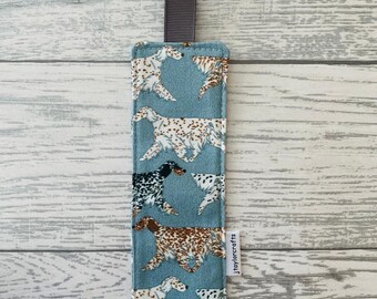 Peut inclure: Un marque-page en tissu bleu avec un motif de chiens blancs et bruns. Le marque-page est doté d'un ruban gris attaché au sommet et du texte "jtaylorcrafts" imprimé sur le côté droit.