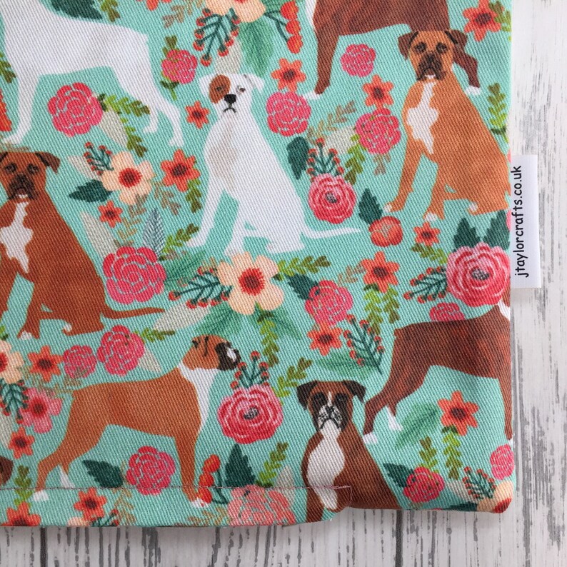 Peut inclure: Un tissu turquoise avec un motif r&eacute;p&eacute;t&eacute; de chiens boxers bruns et blancs et de fleurs roses, rouges et orange. Le tissu a une &eacute;tiquette blanche avec le texte "jtaylorcrafts.co.uk".