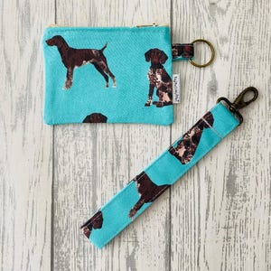 May include: A turquoise zippered pouch and matching key chain with a brown and white dog print. The pouch has a zipper closure and the key chain has a metal ring and a lobster clasp.