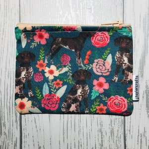 May include: A small, zippered pouch with a teal background featuring a repeating pattern of brown and white dogs and colorful flowers. The flowers are primarily pink and orange. The pouch has a beige zipper and a small white tag that reads "jtaylorcrafts."