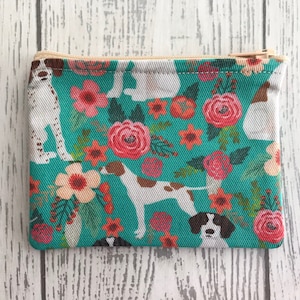 May include: A teal zippered pouch with a white background featuring a repeating pattern of brown and white dogs and colorful flowers.