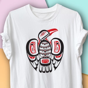 Puede incluir: Camiseta blanca con un diseño estilizado de un pájaro con las alas extendidas en rojo, negro y blanco.