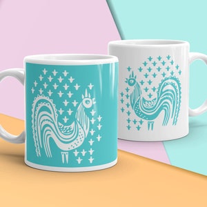 Puede incluir: Dos tazas de cerámica blanca con un diseño de gallo azul turquesa. El gallo está estilizado y tiene un contorno blanco. El fondo de la taza de la izquierda es azul turquesa, mientras que el fondo de la taza de la derecha es blanco con un diseño de gallo azul turquesa.
