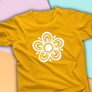 Pode incluir: Uma camiseta amarela com um design floral branco. A flor tem um centro circular e cinco pétalos com detalhes intrincados.