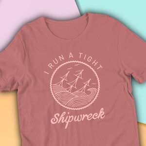 May include: A maroon t-shirt with a white graphic design of a ship in a circle with the text "I run a tight shipwreck".