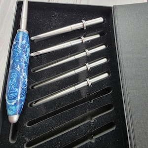 May include: A set of interchangeable crochet hooks in a black presentation box. The set includes one handle with a blue and white marbled resin grip and five metallic hook tips. The text Ocean Crest is printed at the top.