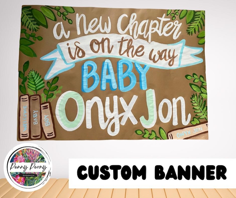May include: A custom banner with the text "a new chapter is on the way BABY Onyx Jon". The banner is brown with white, blue, and green lettering and decorative leaves. The words "Welcome Baby Boy" are on the side.