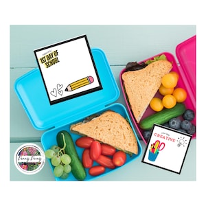 May include: Two open lunchboxes, one blue and one pink, filled with sandwiches, cherry tomatoes, cucumbers, and blueberries. The blue lunchbox has a notepad that says "Happy 1st Day of School" with a pencil and hearts. The pink lunchbox has a notepad that says "You are Creative".