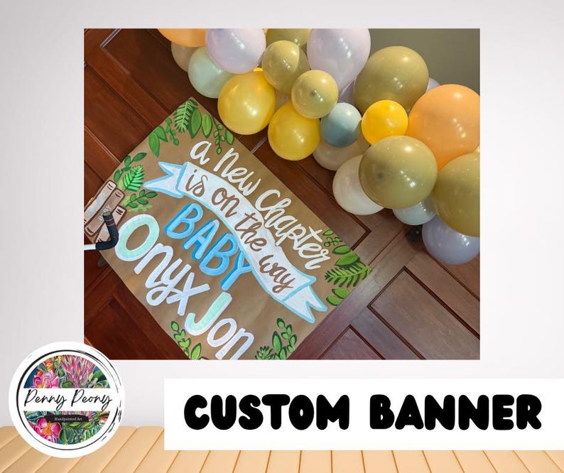 May include: A custom banner with the text "a new chapter is on the way BABY Onyx Jon" in blue and white lettering, with green leaf accents. The banner is surrounded by a colorful balloon arch.