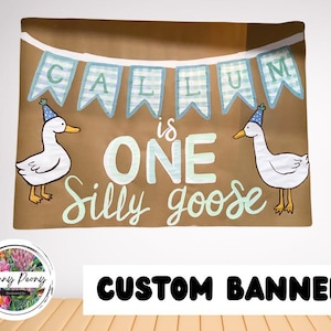 May include: A brown banner with the text "CALLUM is ONE Silly goose" in white and light green. Two cartoon geese wearing party hats flank the text. The banner has a light blue and white checkered banner across the top.
