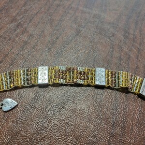 May include: A brown and gold beaded bracelet with silver charms. The charms have a floral design and the words "Forever Friends" are engraved on one of the charms.