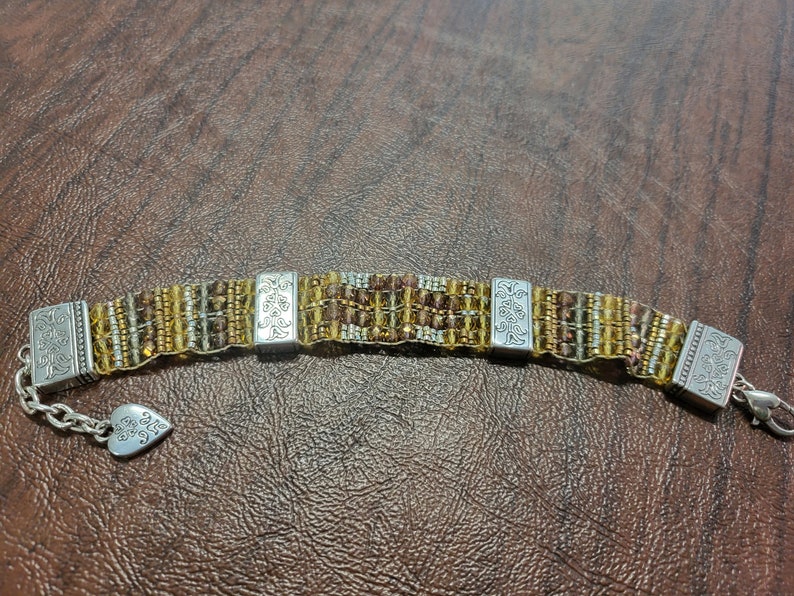 May include: A brown and gold beaded bracelet with silver charms. The charms have a floral design and the words "Forever Friends" are engraved on one of the charms.