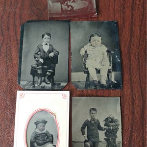 May include: Five vintage black and white photographs of children. Each photo is framed in a white border with a red accent. The photos show children in various poses, including sitting on chairs, standing, and holding objects.