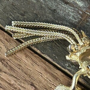May include: A gold-toned brooch with a detailed design and a long, dangling chain of linked metal.