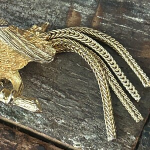 May include: Gold-toned metal brooch featuring a stylized bird with a long, braided tail.