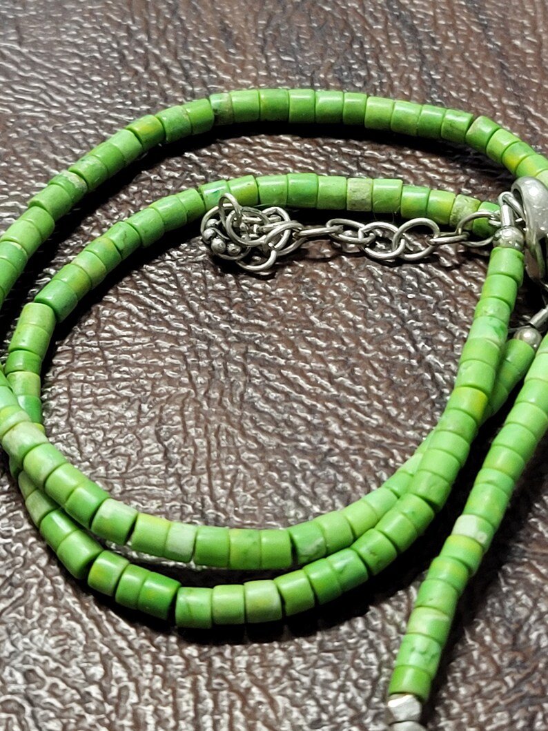 K&ouml;nnte beinhalten: Eine gr&uuml;ne Perlenkette mit einem silbernen Verschluss. Die Perlen sind klein und rund, und die Kette ist etwa 46 cm lang.