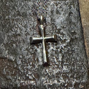 May include: A silver-toned metal cross pendant suspended from a matching fine link chain. The cross features a smooth, polished finish with slightly flared ends on each of the four arms, creating a simple and clean design for this necklace.