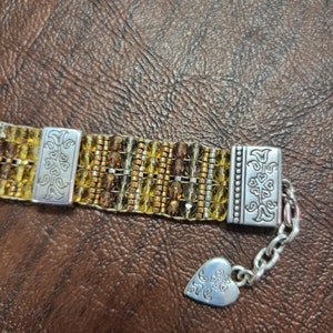 May include: A gold and brown beaded bracelet with silver clasps and a heart-shaped charm with the word "Love" engraved on it.