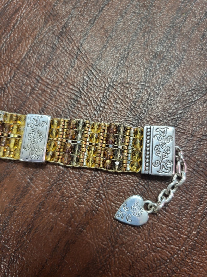 May include: A gold and brown beaded bracelet with silver clasps and a heart-shaped charm with the word "Love" engraved on it.