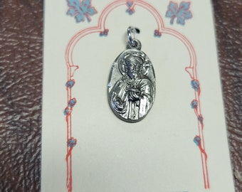 May include: A silver pendant featuring a religious figure with a heart in their hand. The pendant is on a white card with the text "STERLING SILVER RELART".