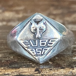 May include: A silver ring with a diamond-shaped face featuring a wolf head and the text "CUBS BSA".
