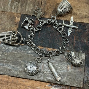 May include: A silver charm bracelet with various charms, including a basket of balls, a whistle, a thimble, a plane, a sewing machine, a watch, and a small building.