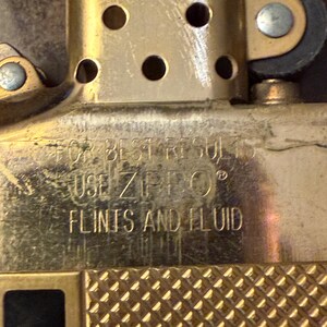 K&ouml;nnte beinhalten: Ein goldfarbener Feuerzeugeinsatz aus Metall mit einem perforierten Kamin und einem strukturierten unteren Bereich. Die Oberfl&auml;che ist mit dem Text FOR BEST RESULTS USE ZIPPO FLINTS AND FLUID graviert, der die f&uuml;r den Betrieb n&ouml;tigen Teile angibt.