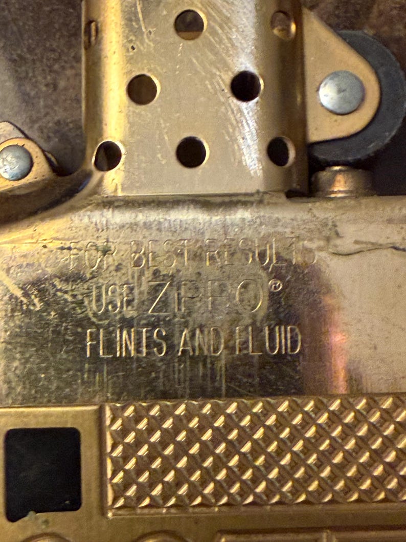 K&ouml;nnte beinhalten: Ein goldfarbener Feuerzeugeinsatz aus Metall mit einem perforierten Kamin und einem strukturierten unteren Bereich. Die Oberfl&auml;che ist mit dem Text FOR BEST RESULTS USE ZIPPO FLINTS AND FLUID graviert, der die f&uuml;r den Betrieb n&ouml;tigen Teile angibt.