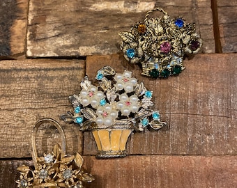 Puede incluir: Tres broches vintage de tono dorado con arreglos florales en cestas. Los broches están adornados con pedrería y perlas falsas.