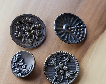 May include: Four antique metal buttons with intricate designs. The buttons are round and have a silver and gold finish. The designs include floral patterns, geometric shapes, and a stylized sunburst.
