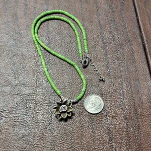 K&ouml;nnte beinhalten: Eine gr&uuml;ne Perlenkette mit einem silbernen Blumenanh&auml;nger. Die Kette ist etwa 45 cm lang und der Anh&auml;nger etwa 2,5 cm im Durchmesser.