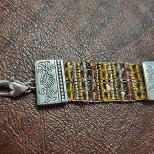 May include: A gold and brown beaded bracelet with a silver clasp. The clasp has a floral design.