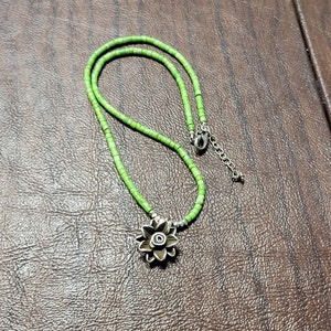 K&ouml;nnte beinhalten: Eine gr&uuml;ne Perlenkette mit einem silbernen Blumenanh&auml;nger. Die Kette besteht aus kleinen, runden Perlen und hat ein schlichtes, elegantes Design.