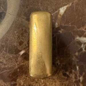 K&ouml;nnte beinhalten: Ein rechteckiger, goldfarbener Metallriegel mit abgerundeten Ecken und einer glatten, leicht verwitterten Oberfl&auml;che. Das Objekt hat eine solide, l&auml;ngliche Form mit einem gleichm&auml;&szlig;igen metallischen Finish und feinen Gebrauchsspuren.