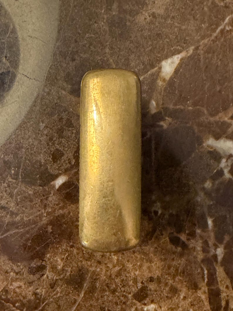 K&ouml;nnte beinhalten: Ein rechteckiger, goldfarbener Metallriegel mit abgerundeten Ecken und einer glatten, leicht verwitterten Oberfl&auml;che. Das Objekt hat eine solide, l&auml;ngliche Form mit einem gleichm&auml;&szlig;igen metallischen Finish und feinen Gebrauchsspuren.