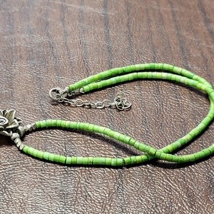 K&ouml;nnte beinhalten: Eine gr&uuml;ne T&uuml;rkis-Perlenkette mit einem silbernen Blumenanh&auml;nger.