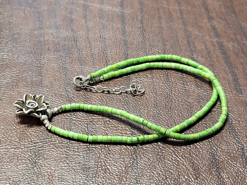 K&ouml;nnte beinhalten: Eine gr&uuml;ne T&uuml;rkis-Perlenkette mit einem silbernen Blumenanh&auml;nger.