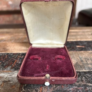 May include: A small, burgundy velvet-lined jewelry box with a hinged lid and a white button closure.
